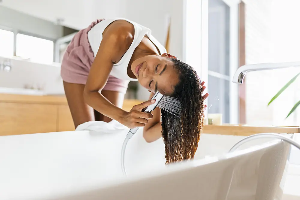 Women in bathroom washing her brown long hair in bath tube